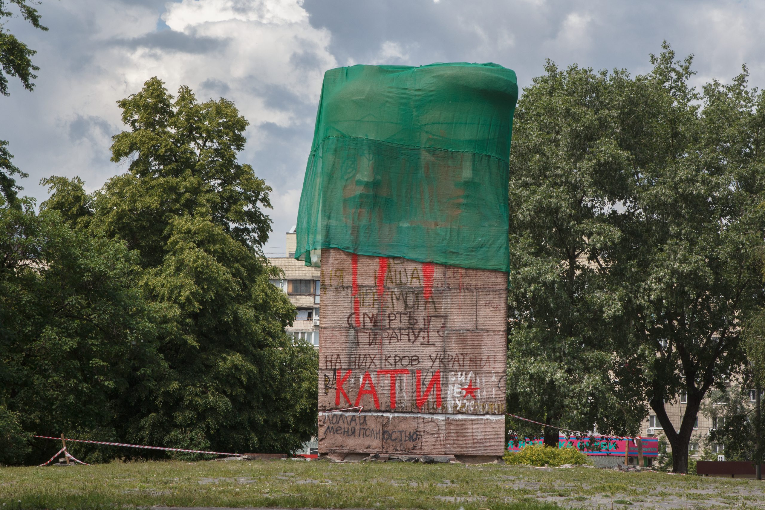 large Soviet World War 2 Red Army monument with graffitti covered by a green cloth in an urban park